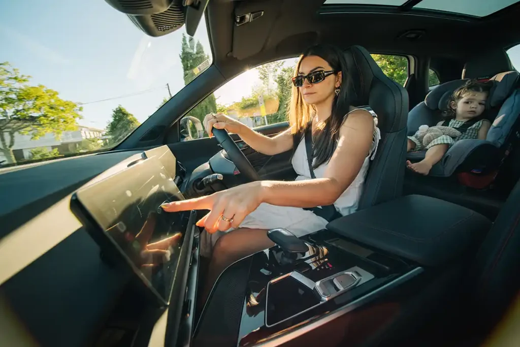 Woman in the driver's seat of a BAIC X55 SUV pressing the centre touchscreen with her baby in a child seat sitting in the second row