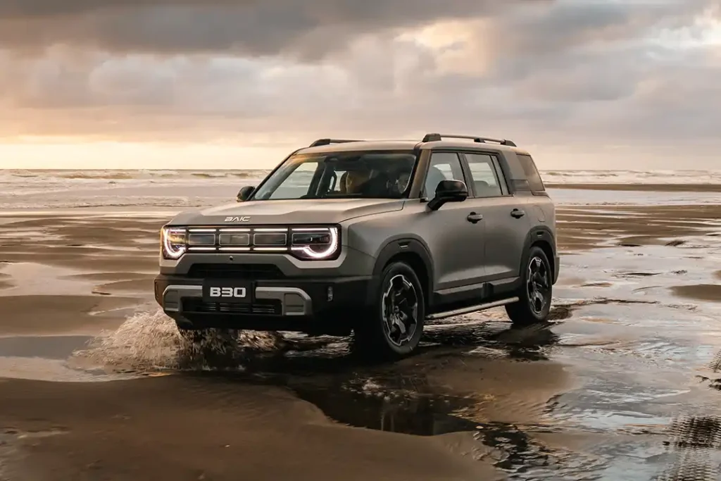 Front three quarter view of a dark grey BAIC B30 SUV driving on the wet sand on a New Zealand beach