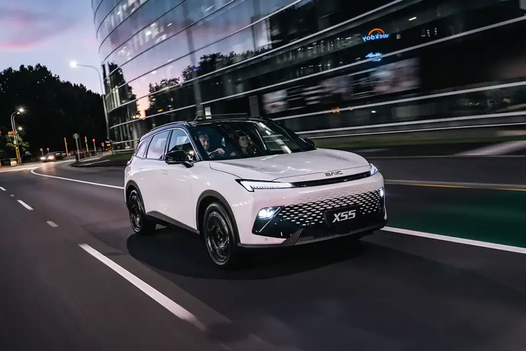 Front three quarter view of a white BAIC X55 SUV driving through Auckland city at night