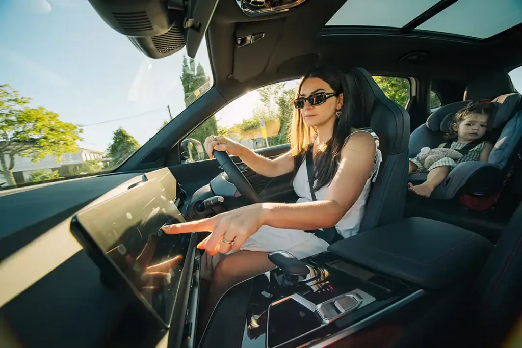 Interior view of a BAIC X55 SUV with a woman sitting in the driver seat and touching the centre screen, with her toddler in a car seat in the rear