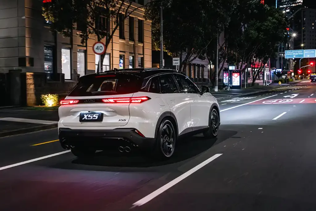 Rear three quarter view of a white BAIC X55 SUV driving through Auckland city at night