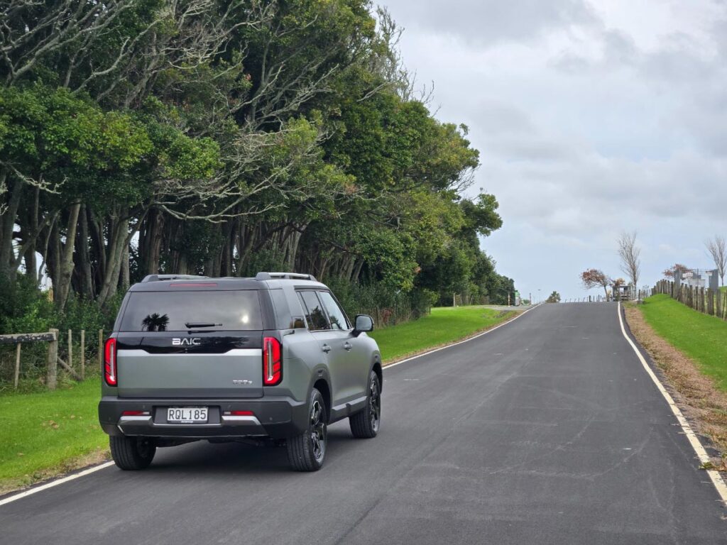 Rear view of a silver BAIC B30 hybrid SUV driving on a country road