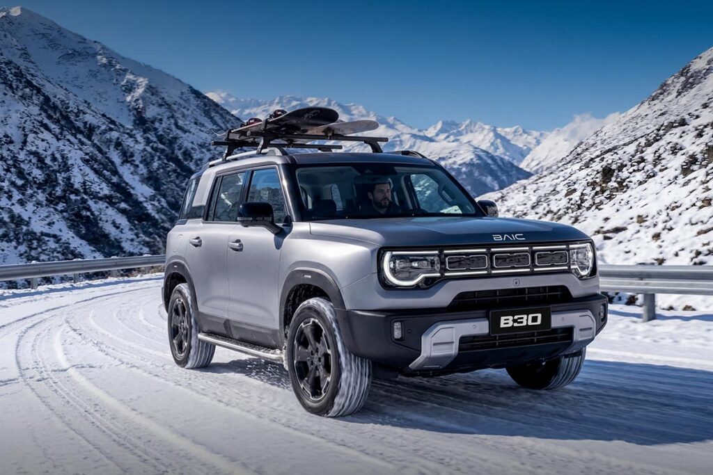 Front three quarter view of a silver BAIC B30 Hybrid SUV driving across a snow covered road in the mountains with snowboards on its roof racks
