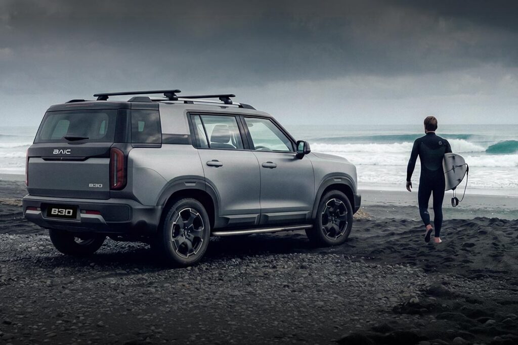 Rear three quarter view of a silver BAIC B30 Hybrid SUV parked at the beach with a surfer standing nearby
