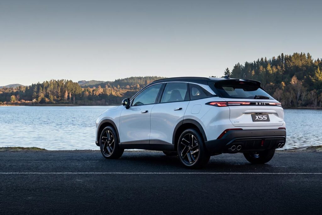 Rear three quarter view of a white BAIC X55 SUV parked in front of a lake in the early morning