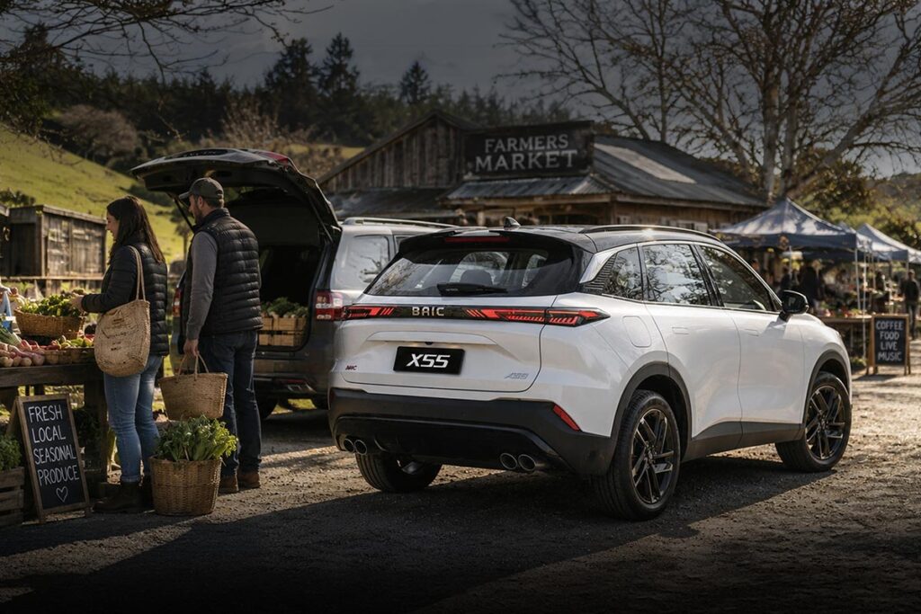 Rear three quarter view of a white BAIC X55 SUV parked at a farmers market with people shopping at various stalls
