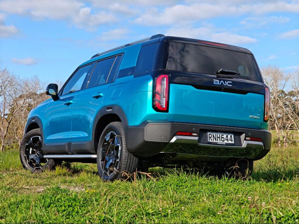 Rear three quarter view of a blue BAIC B30 SUV Premium Adventure Hybrid AWD parked in a field